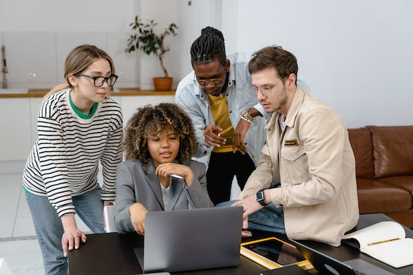 A photo showing office employees gathered around a laptop.