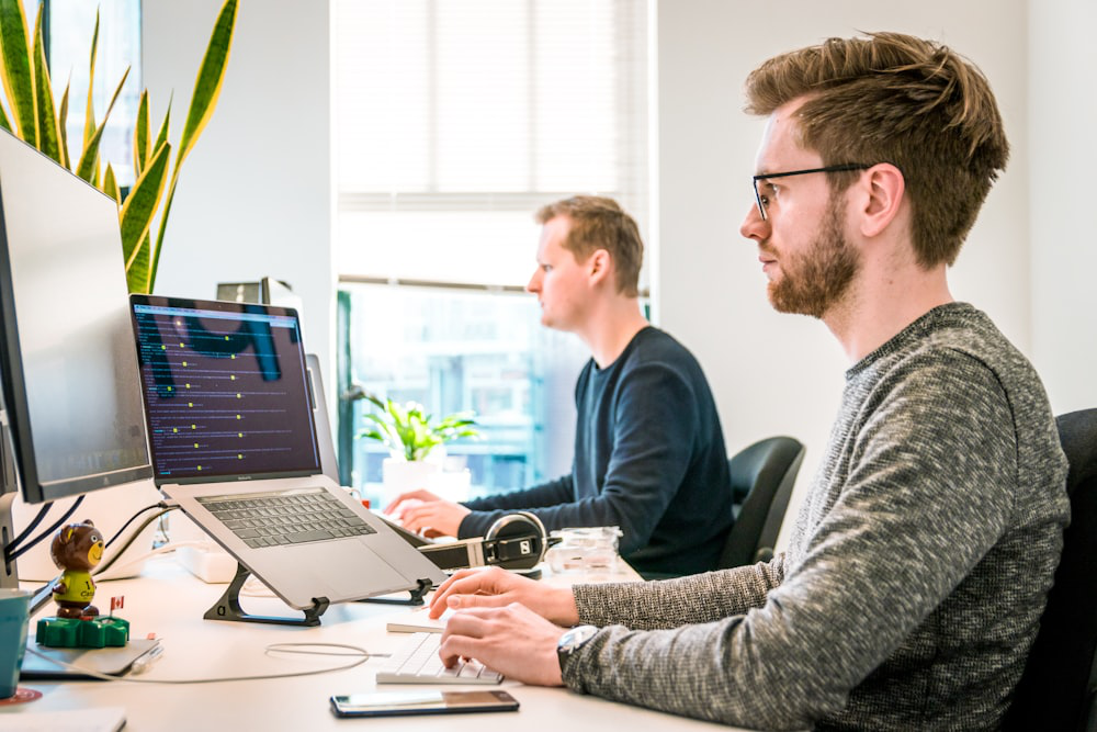 A photo of people using a computer and a laptop in an office     