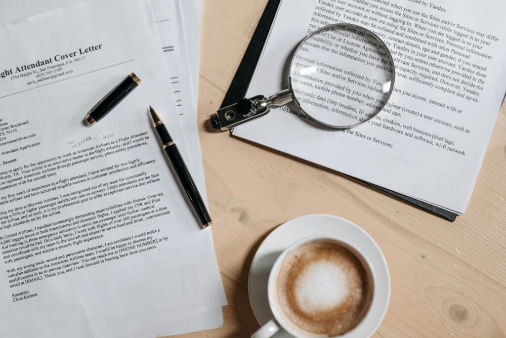 A picture of a cover letter, a cup of coffee, and a magnifying glass against a wooden surface